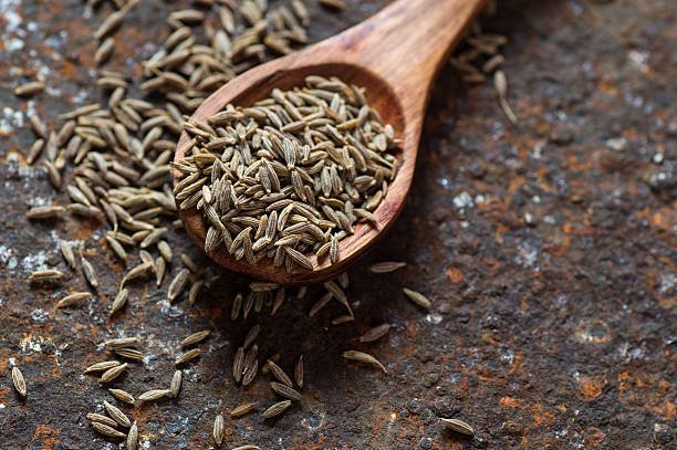 Cumin seeds in wooden spoon on texture background
